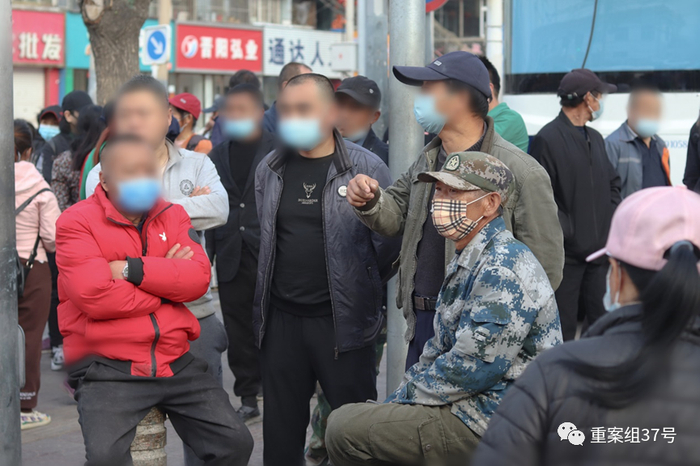 ▲4月12日早上7点半，身穿迷彩服的姜兴申和一些同样在“蹲活”的人在马路边闲谈。  新京报实习生汤赛坤 摄