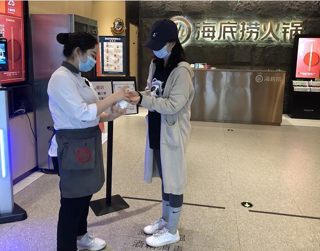 图为海底捞门店防疫站，店员为顾客测温消毒