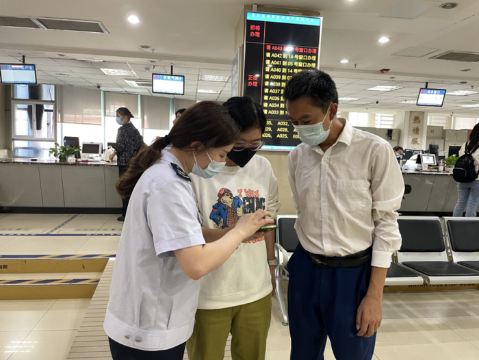 ▲在沙坪坝区不动产登记中心，税务人员辅导市民使用手机下载契税完税证明。重庆市税务局供图