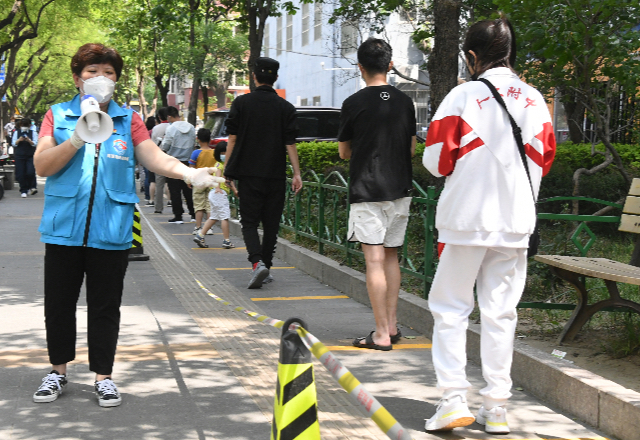 5月5日，在北京市海淀区中关村街道东里南社区临时核酸检测采样点，社区工作人员（左一）引导市民有序排队。新华社