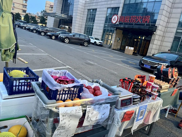 ▲5月23日傍晚，海底捞万丰桥店停车场入口。摊位上摆满了果蔬、鸡蛋、火锅底料、方便食品等。新京报记者 吴淋姝 摄