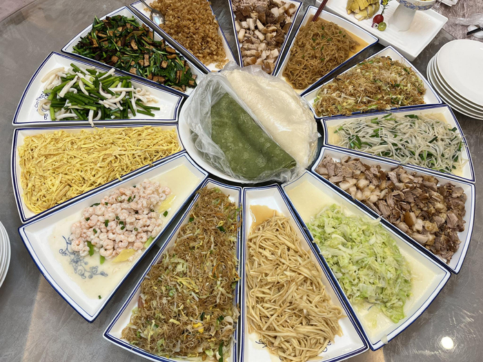 一桌拼盘，盛满五花八门十几道菜肴，菜肴中间是两大盘面皮，一青一白。