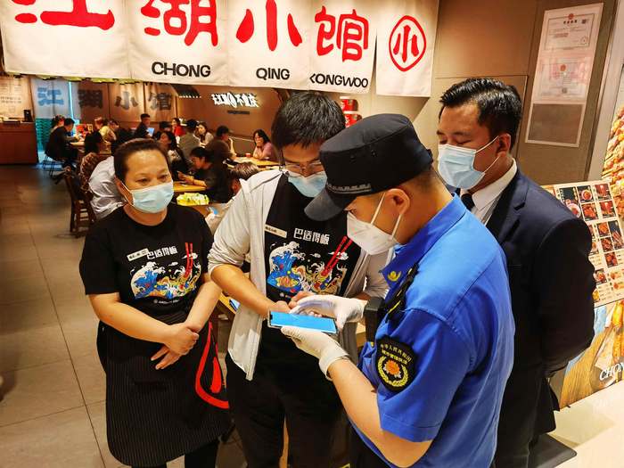 综合执法队负责人和购物中心的工作人员，正在查验商户的健康宝数据。