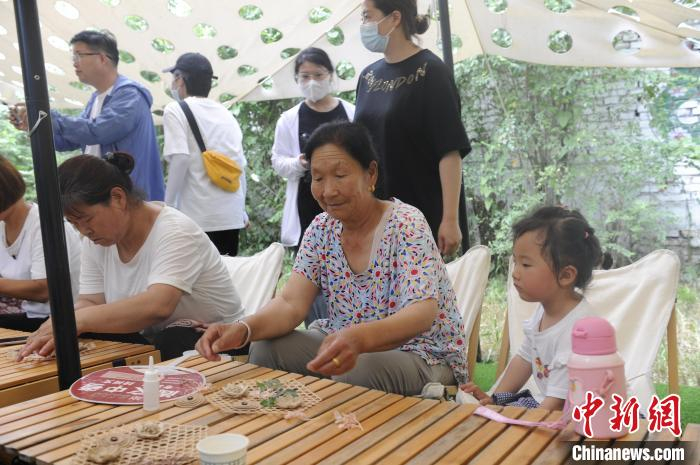 图为乔村的妇女向孩童讲解制作手工艺品的要点。　高铖 摄
