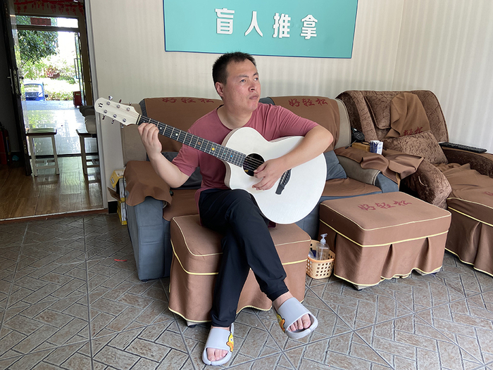 为了打发时间，盲人按摩师任凤来在店里练习吉他。