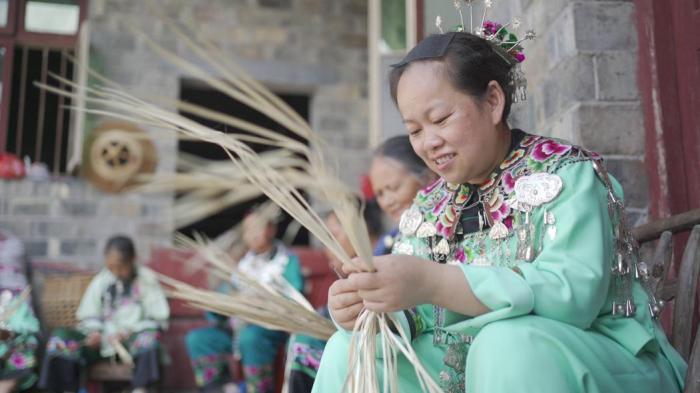 ▲在吉信镇的苗族村子里，黄明芳与老人们一起编织蒲扇。