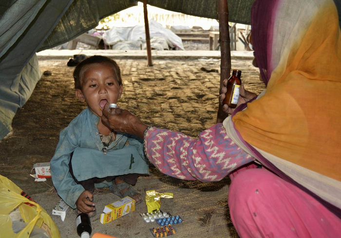 当地时间2022年9月2日，巴基斯坦旁遮普省拉詹普尔地区，在灾区帐篷里，一名妇女在给儿子吃药。