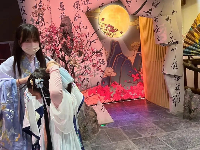  ▲2022年10月30日下午2点，在沉浸式主题商业空间“戏精桃花源”入口处的服装店外，NPC（非玩家角色工作人员） 帮小朋友换上汉服，整理发饰。新京报记者 杨柳 摄