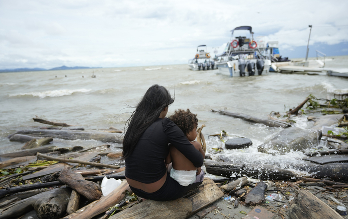 当地时间2022年10月13日，哥伦比亚Necocli，委内瑞拉移民Yusney Velandia和她的孩子看着从哥伦比亚Necocli前往阿坎迪的移民船只，她正在考虑继续她的北上之旅。