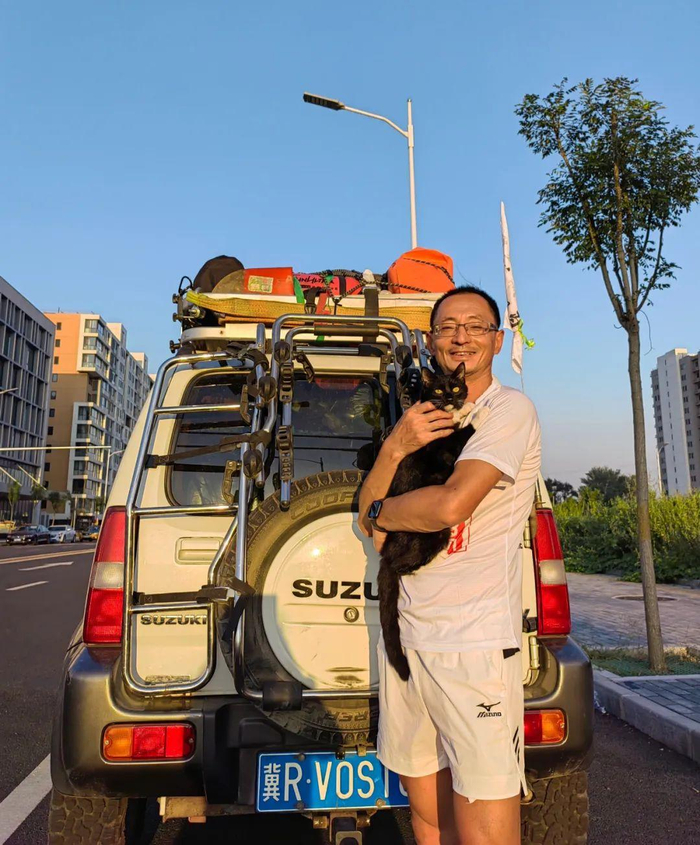 出发前，樊龙智抱着小妖与满载物资的保障车合影。受访者供图