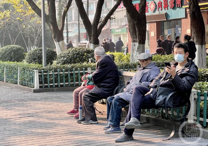 ▲中心城区周六暖阳当空，不少市民坐在路边晒太阳