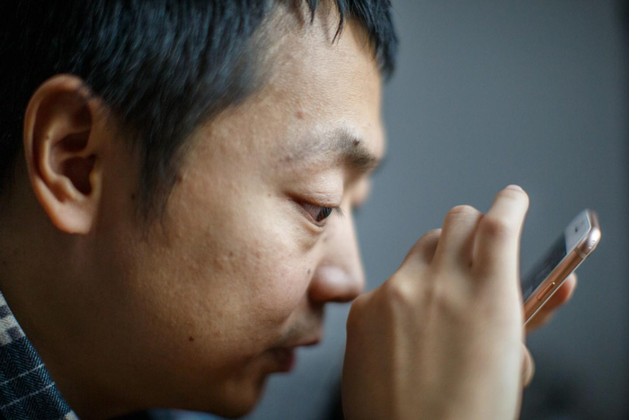 蔡聪在家中用手机寻找照片，照片无法转化成语音，他只能努力靠近屏幕辨别画面。新京报记者 王子诚 摄