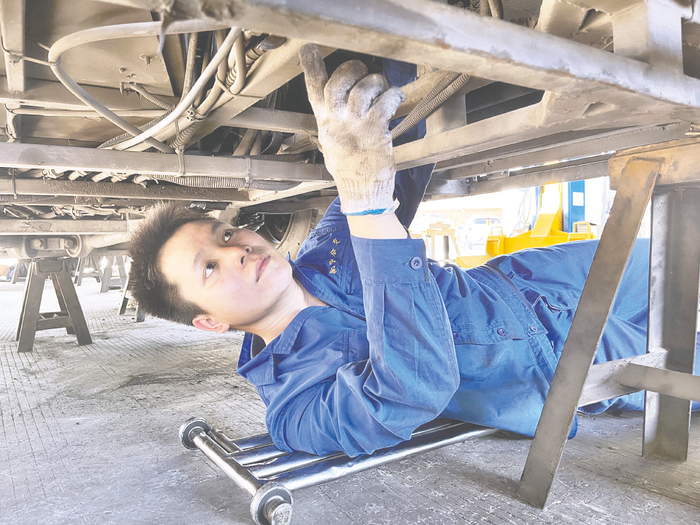     黄振安钻入车底检查公交车底盘。    （周天心 摄）
