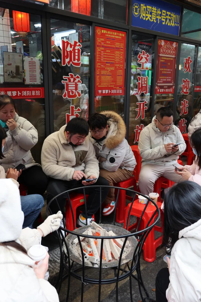 1月15日，长沙。笨萝卜浏阳菜馆门前坐满了排队的食客，大家围着火炭盆取暖。/林泽君