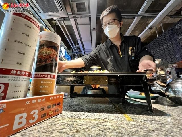 2月12日，红山路疯鱼军团餐厅里，服务员为顾客上菜，桌上摆放着“文明餐桌厉行节约”的提示语。记者王畅彤摄