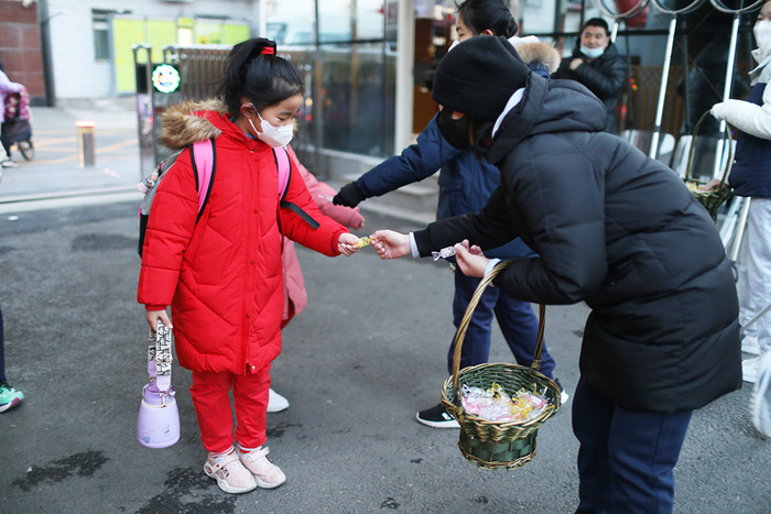 2023年2月13日，北京，北京市十一学校一分校，学校老师给入校学生分发糖果。风依/澎湃影像 图