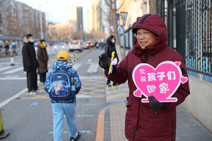 2023年2月13日上午，北京小学通州分校门口，学校教师在校门口举牌迎接学生们返校。视觉中国 图