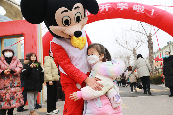 2023年2月7日，山东省高密市金苹果幼儿园的孩子在入校时与卡通人偶拥抱。新华社发（李海涛 摄）