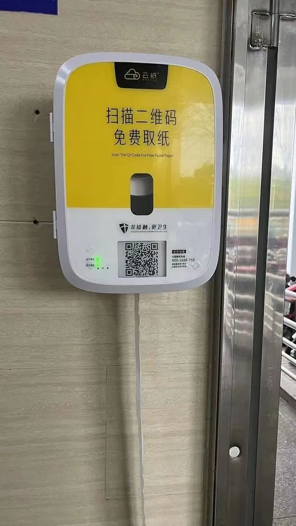 　　公厕进门墙上写着“提供应急厕纸”提示，下方安装着一个自动取纸机，黄白色的自动取纸机上写着“扫描二维码，免费取纸”。受访者供图