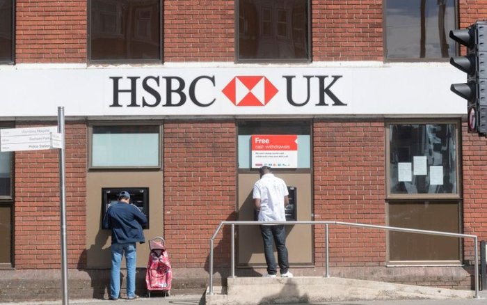 资料图。人们在英国伦敦的一家汇丰银行外操作ATM机。图/新华社