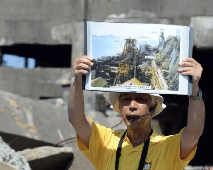 　　▲2015年8月8日，在日本长崎“军舰岛”，导游讲解岛上历史。“二战”期间，曾有大量来自朝鲜半岛和中国的劳工被强征到这座小岛上劳动。图/新华社