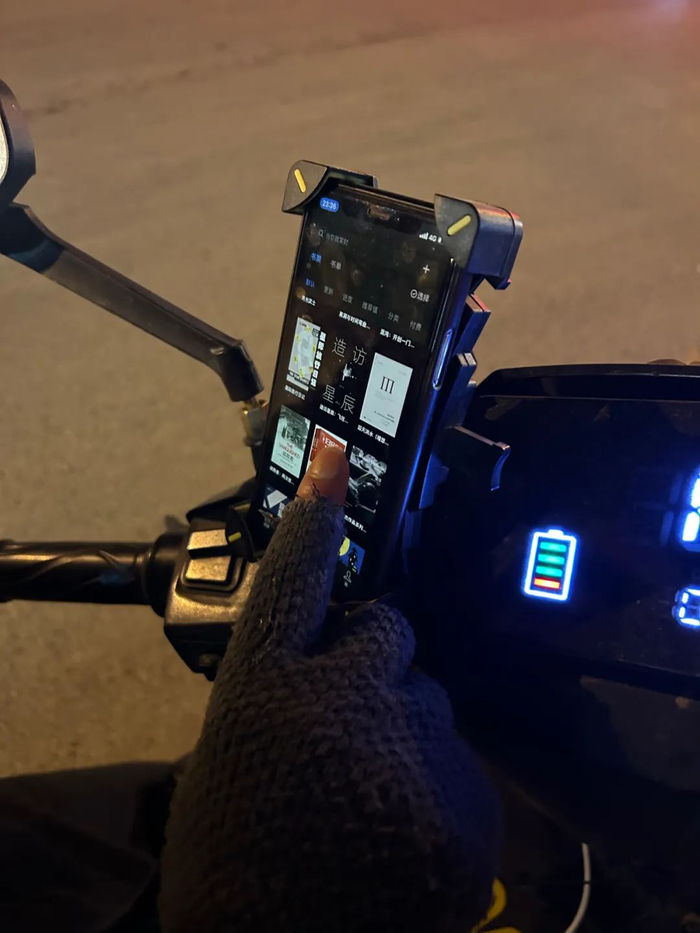 ▲等单子的期间，陈涛会在路边用手机看一些有关于社会科学和科幻的书。新京报记者 侯庆香 摄