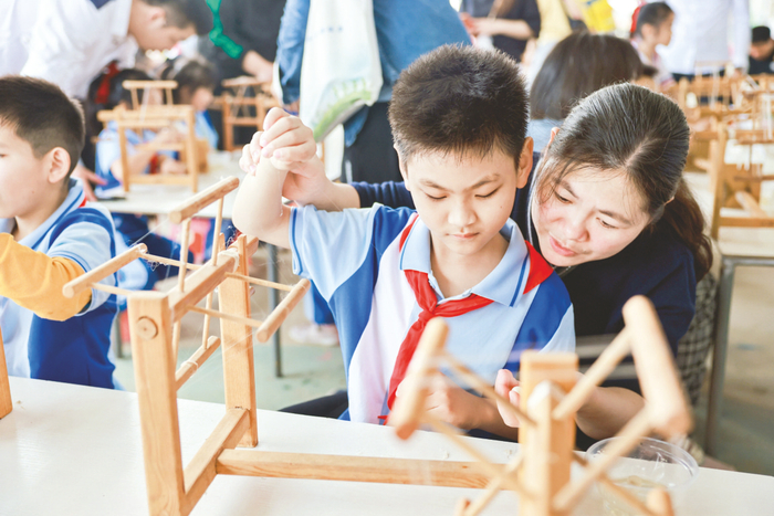     ▲南宁市月湾路小学学生和家长一起尝试抽取蚕丝。 （邓楚红 摄）