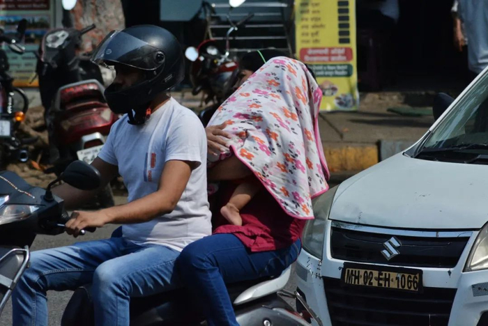 当地时间2023年4月19日，印度孟买，一名妇女坐在电动车后座，她在闷热的午后遮住了孩子的头和脸。图/视觉中国