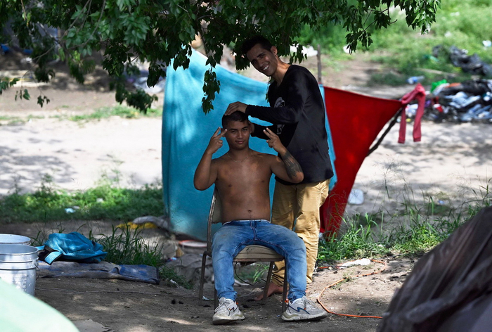 当地时间5月9日，墨西哥马塔莫罗斯，格兰德河岸边的临时营地里，一名男子在理发时向镜头挥手。