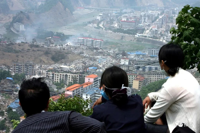 ▲2008年5月22日，几位群众在被地震摧毁的北川县城边的山坡上，遥望自己曾经的家园。摄影 / 何龙盛