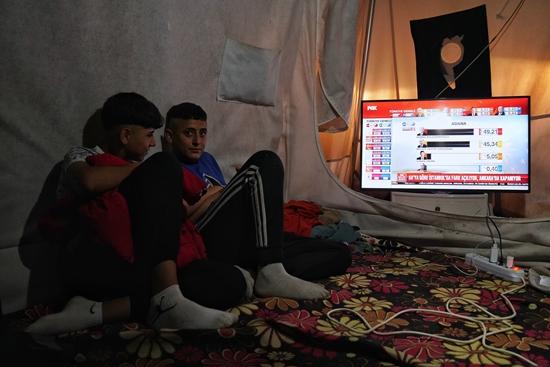     5月14日，土耳其哈塔伊，人们在地震灾区帐篷里观看土耳其总统选举第一轮投票结果的报道。视觉中国供图