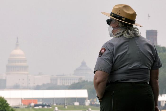 6月29日，在好意思国齐门华盛顿，国度公园的别称职工戴着口罩责任，远方的国会大厦笼罩在烟雾中。
