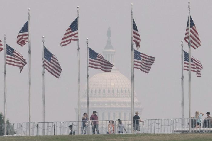 6月29日，在好意思国齐门华盛顿，旅客在华盛顿挂牵碑游览，远方的国会大厦笼罩在烟雾中。