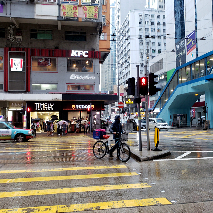 香港铜锣湾街头，一位外卖骑手冒雨骑单车送货。图源：麻吉 摄
