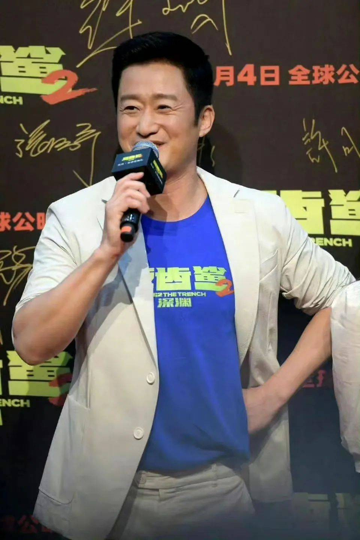 当天,吴京身穿印有巨齿鲨字样的蓝色t恤,穿着一套白色西装,笑容满面地