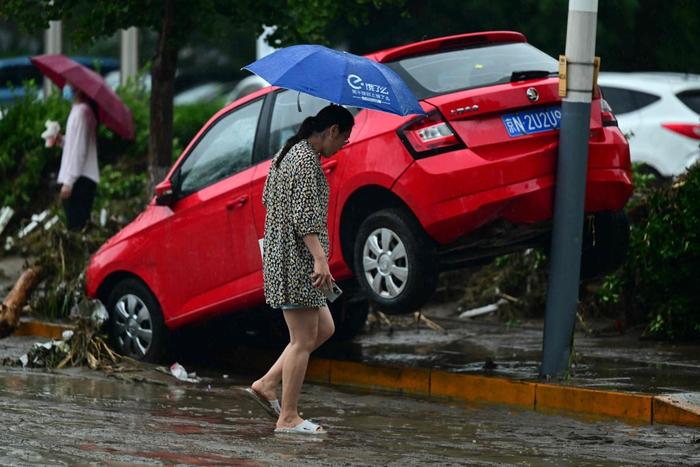 7月31日，北京门头沟区，暴雨过后，一名妇女路过一辆受损抛锚的汽车。
