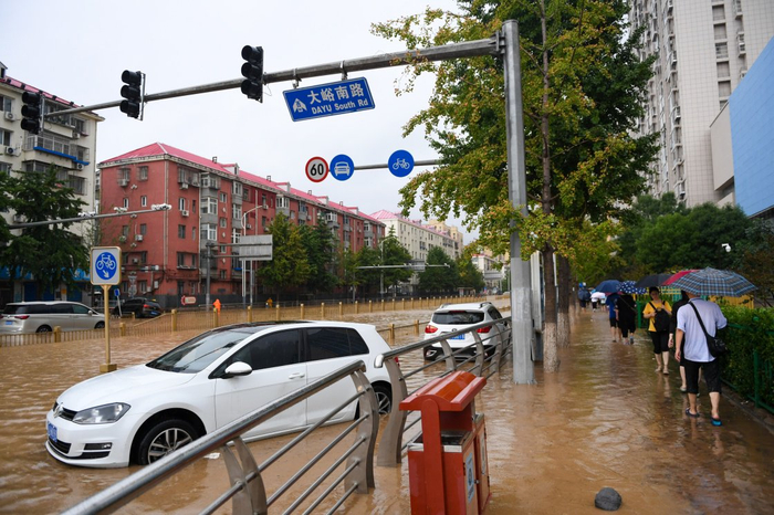 7月31日，在北京市门头沟区大峪南路，行人从积水的路面和泡水的车辆旁走过。新华社 图