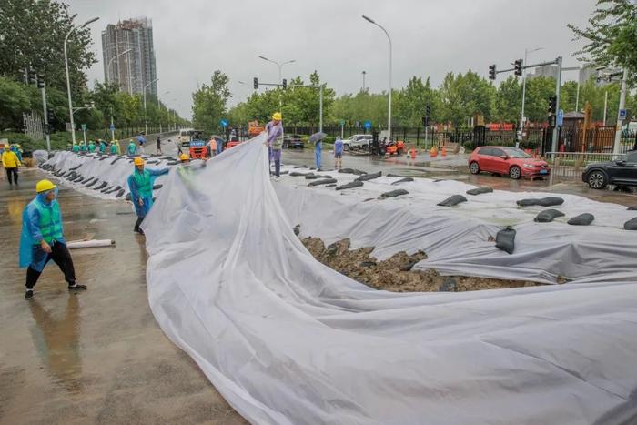 ▲7月30日上午，北京通州区紫运西路，工人正在添加防雨布加固堤坝。新京报记者 王子诚 摄