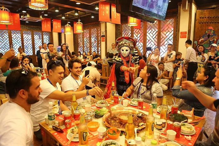 现在，中华饮食文化的代表火锅风靡海内外。图为外国友人品尝成都火锅，观看川剧变脸。（图片来源：视觉中国）