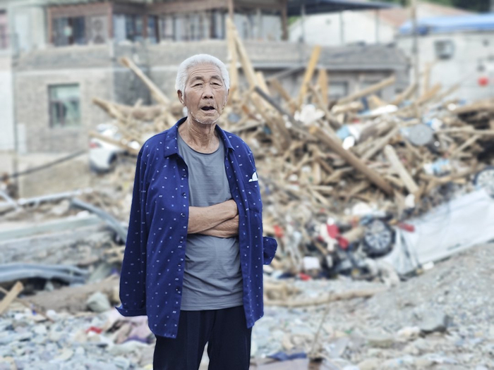 8月13日，北京门头沟，受灾后的王平镇，东马各庄村一位老人站在废墟边上，看着救援队进行清淤、疏通道路作业。