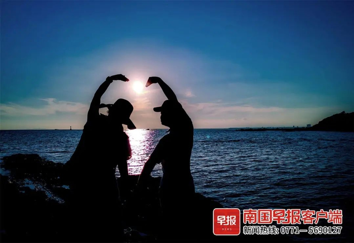 ▲在防城港市的怪石滩，一对情侣对着落日比出爱心形状。南国早报全媒体记者 游拥军摄