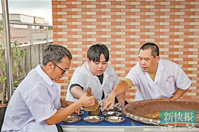 ▲梁毅兴（右一）在指导徒弟学习膏药制作技艺。