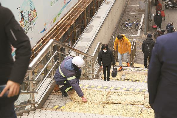             彭浦新村地铁站外，工作人员正在铺设防滑草垫  本报记者  李铭珅  摄          