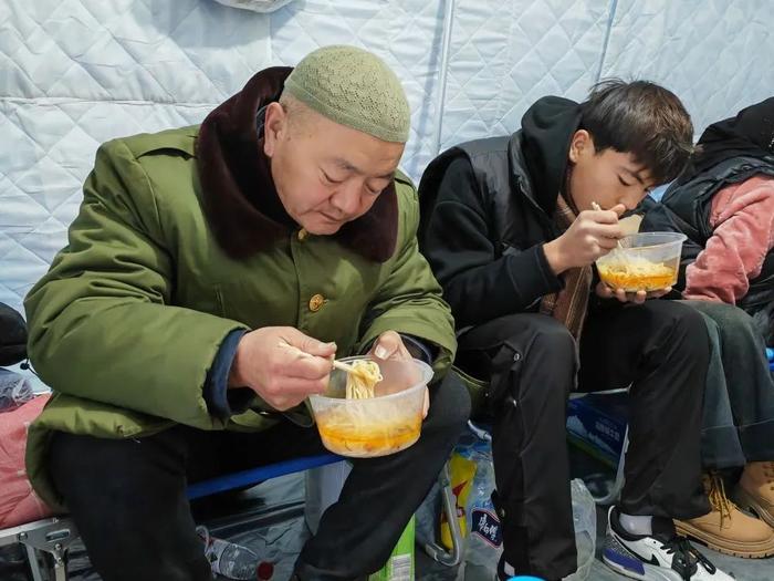 在安置点的帐篷里,马仲明(左一)和同村村民正在吃面。新华社记者 胡伟杰 摄