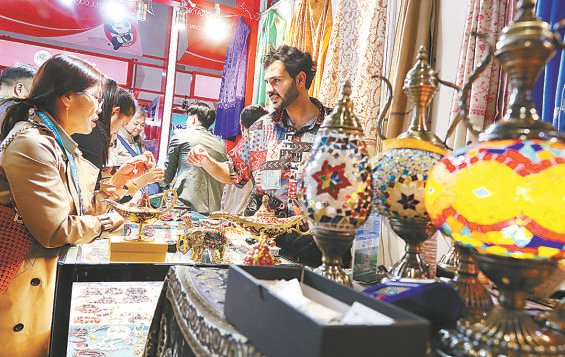 11月10日，在第六届进博会上，一名来自也门的展商（右）向观众介绍特色手工艺品。 新华社发