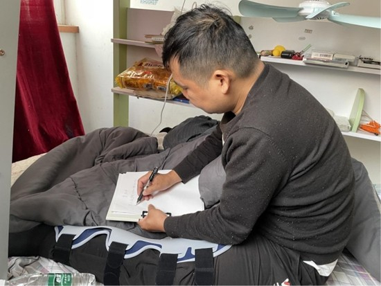     向建军坐在租屋的床上写材料。受访者供图