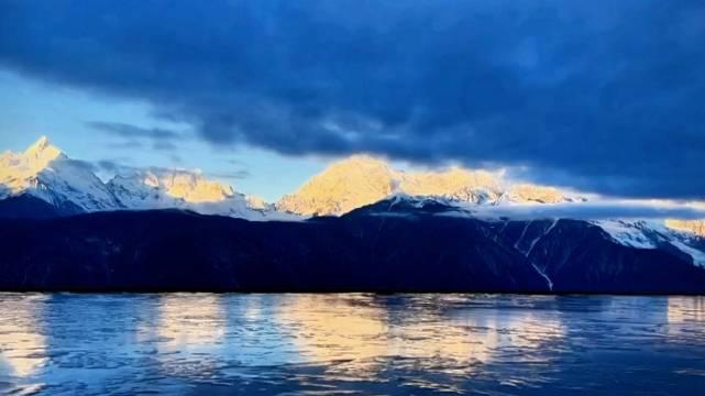 夢幻般的藍色調陽光從雲層中灑落照亮了雪山之巔金光閃爍周圍的山巒在