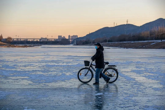 2024年1月15日，门头沟区龙泉镇龙泉雾村，一位村民在结冰的永定河上推着自行车过河。