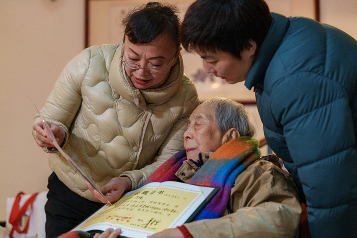 ▲2月5日，肖鸣锵家中，肖鸣锵（中）接受收藏证书。见习记者 李雨恒 摄