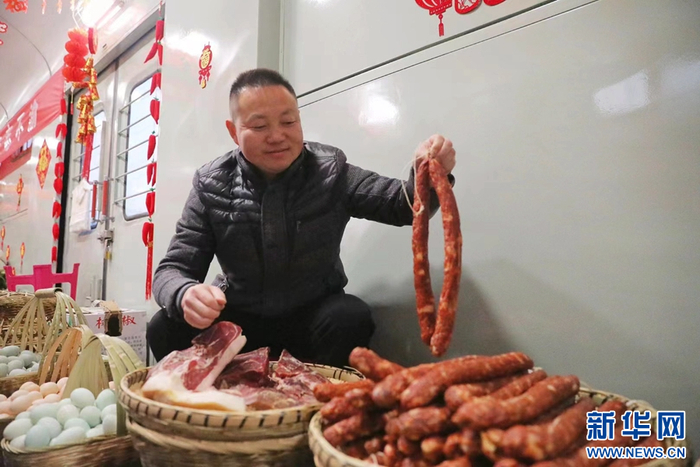 2月2日，“慢火车”年货街上，一名摊主展示售卖的腊肉和香肠。图源：新华网（杨紫轩 摄）